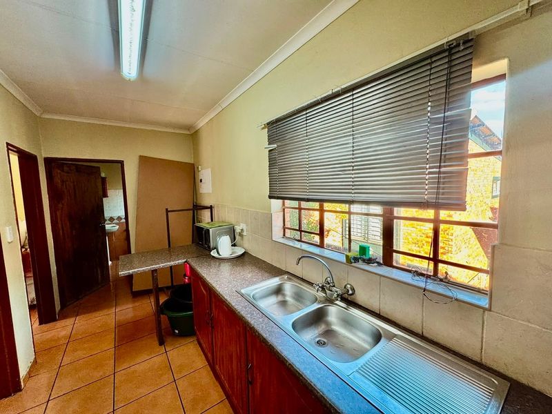 A functional kitchen featuring wooden cabinetry, a double bowl stainless steel sink, tiled flooring, and a window with blinds providing natural light.