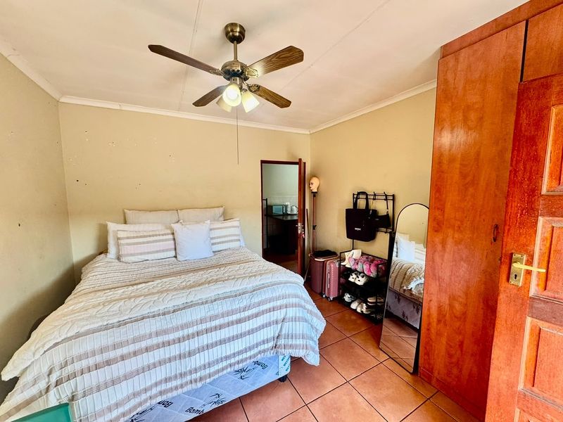 A bedroom featuring tiled flooring, a ceiling fan, and a built-in wooden wardrobe, offering a functional space with potential for cosmetic updates.