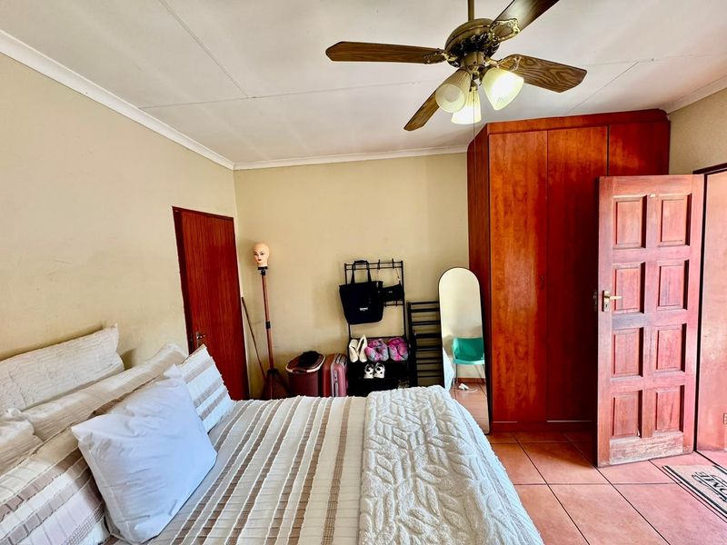 A bedroom featuring a ceiling fan, built-in wooden wardrobe, and tiled flooring, offering a functional space with potential for cosmetic updates.