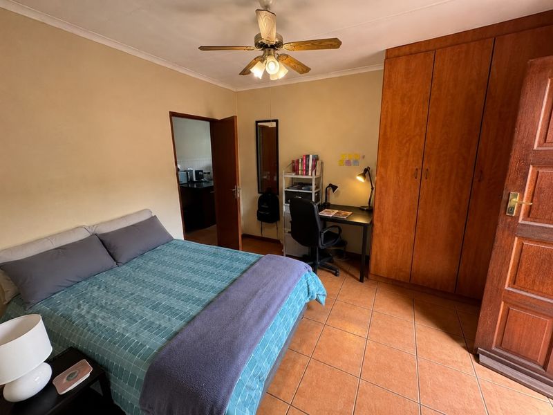 A functional bedroom featuring tiled flooring, a built-in wooden wardrobe, and a ceiling fan, with direct access to an adjacent room.