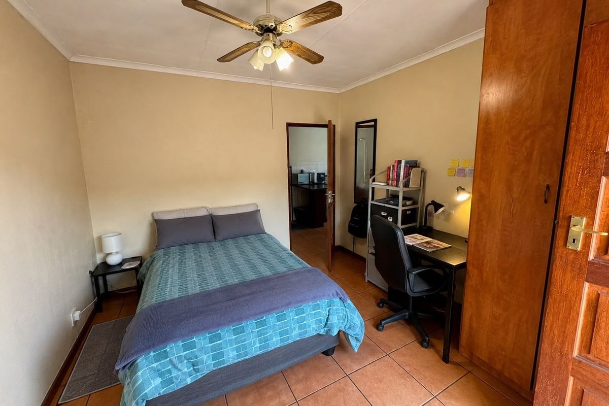 A functional bedroom featuring tiled flooring, a ceiling fan, and a built-in wooden wardrobe, with direct access to an adjacent room.