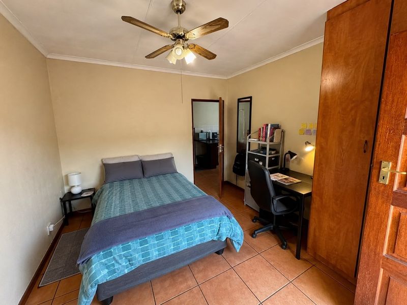 A functional bedroom featuring tiled flooring, a ceiling fan, and a built-in wooden wardrobe, with direct access to an adjacent room.