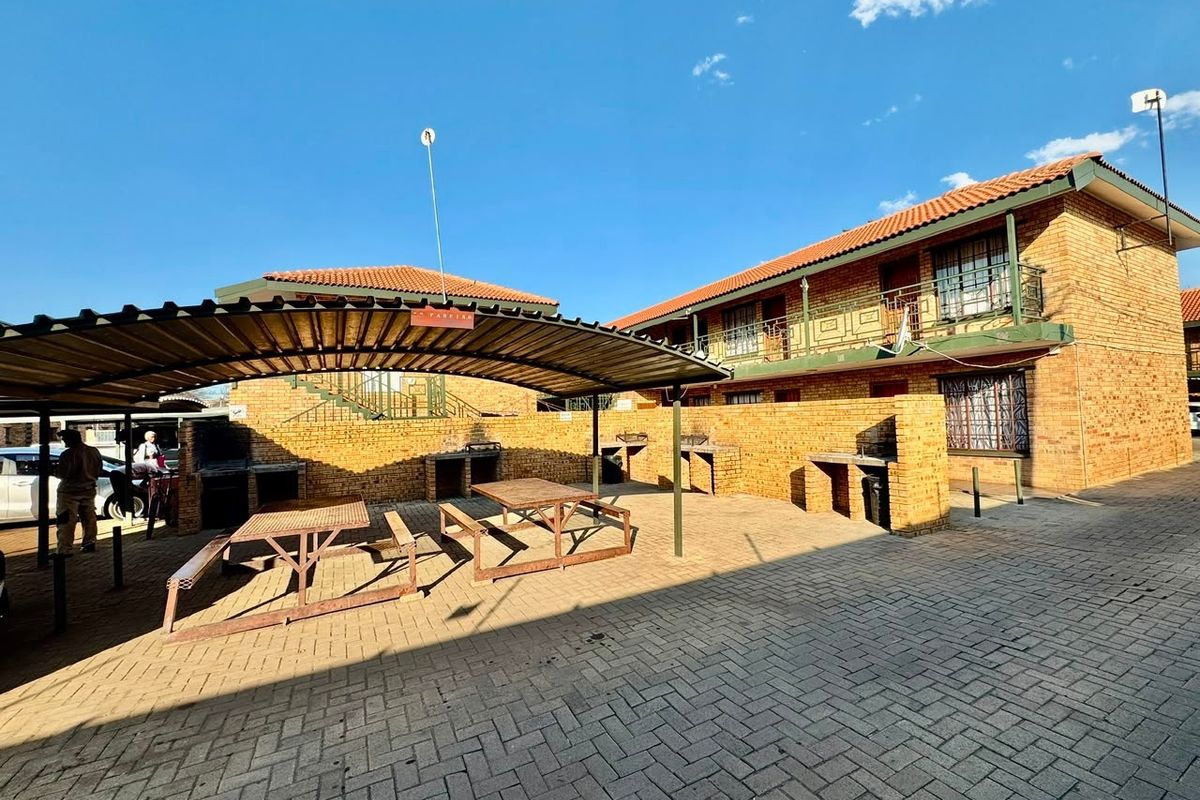 Communal outdoor area featuring brick paving, a covered carport structure, and multiple built-in braai stations for resident use.