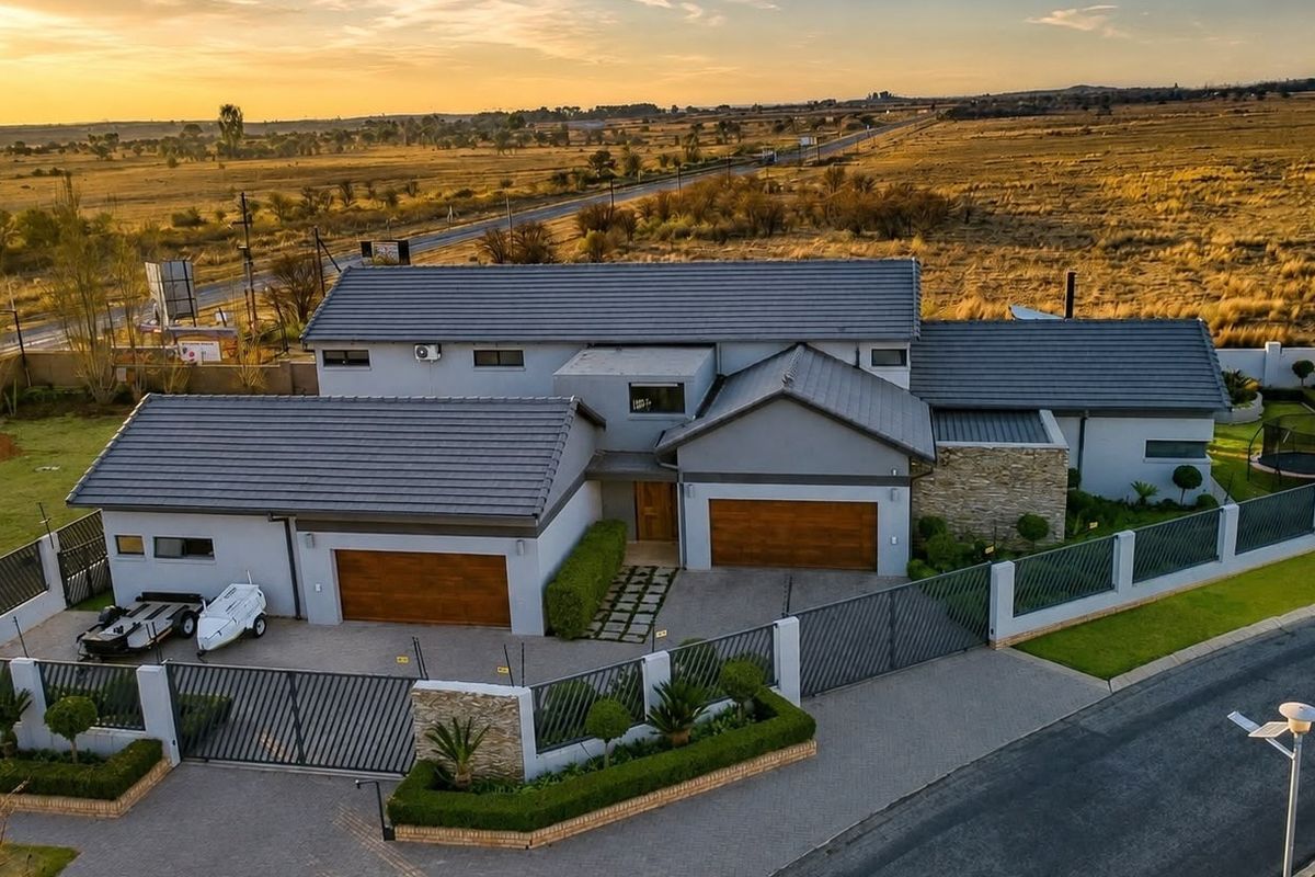Aerial view of a modern residential property featuring a tiled roof, double garage, paved driveway, and secure perimeter walling in a landscaped setting.