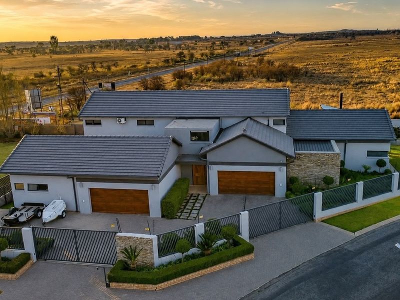 Aerial view of a modern residential property featuring a tiled roof, double garage, paved driveway, and secure perimeter walling in a landscaped setting.