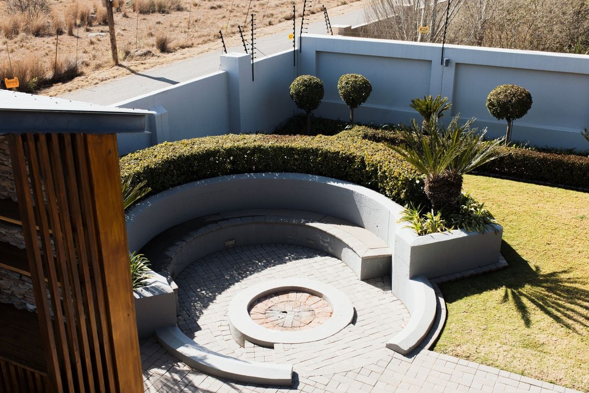 A well-maintained rear garden featuring a paved circular fire pit area with built-in concrete seating, surrounded by landscaped hedges and a secure perimeter wall.