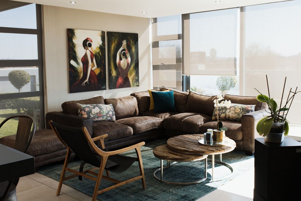 A bright and modern living room featuring large windows with roller blinds, recessed downlighting, and neutral tiled flooring.