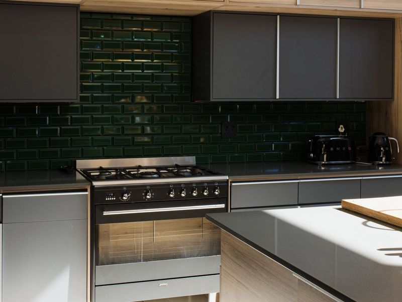 Modern kitchen featuring dark cabinetry, a gas stove with oven, a striking green subway tile backsplash, and a stone-topped kitchen island.