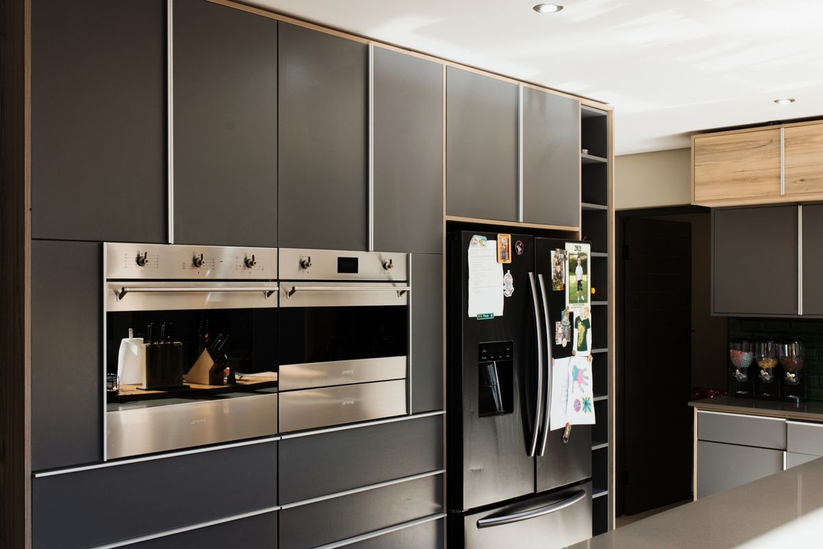 Modern kitchen featuring sleek dark cabinetry, built-in double ovens, stone countertops, and a stylish subway tile backsplash with integrated lighting.