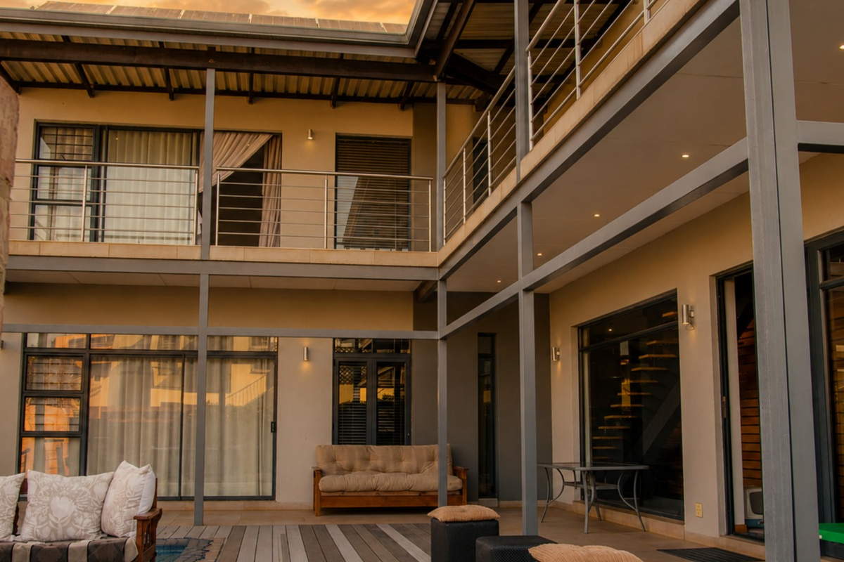A modern double-story rear exterior featuring a spacious covered patio, steel structural elements, and large sliding glass doors providing seamless indoor-outdoor flow.