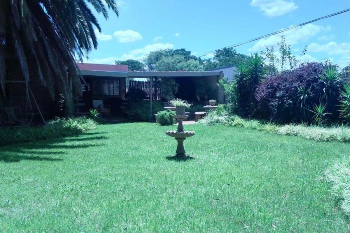 A spacious rear garden featuring a well-maintained lawn, a central stone fountain, and a covered patio area.