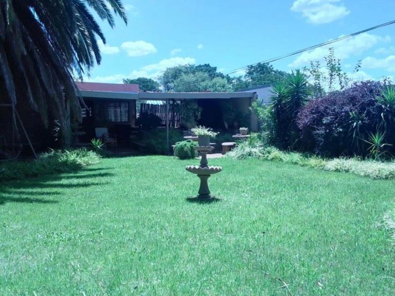 A spacious rear garden featuring a well-maintained lawn, a central stone fountain, and a covered patio area.