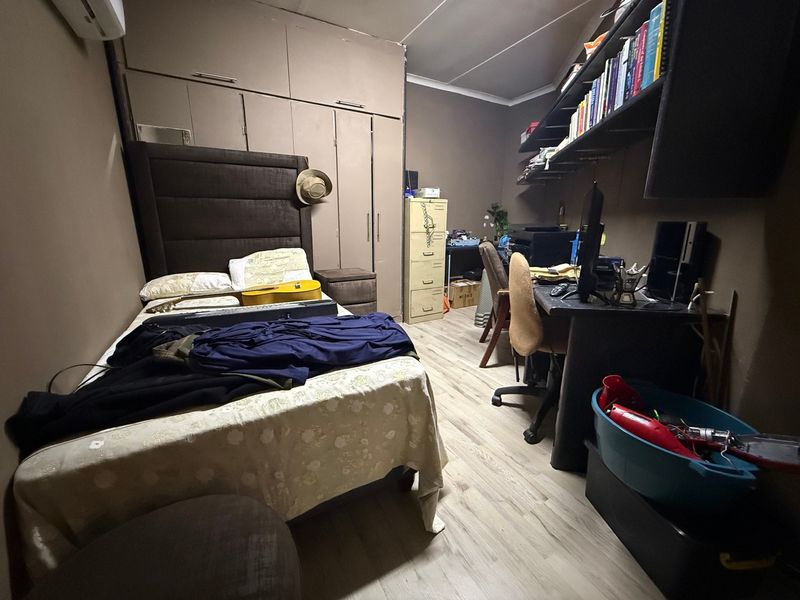 A functional bedroom featuring built-in cupboards, laminate flooring, and a wall-mounted air conditioning unit, offering practical storage and climate control.