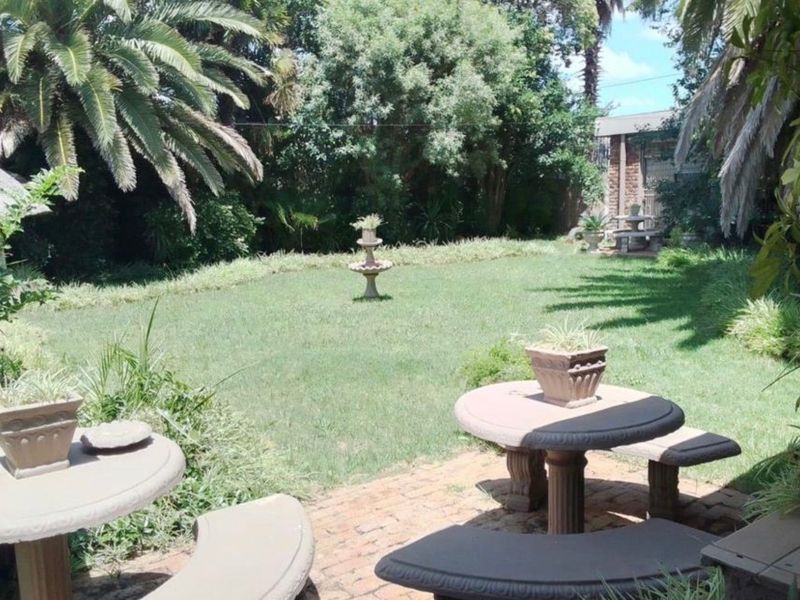 A lush, private garden featuring a central stone fountain, mature trees, and a brick-paved patio area perfect for outdoor relaxation.