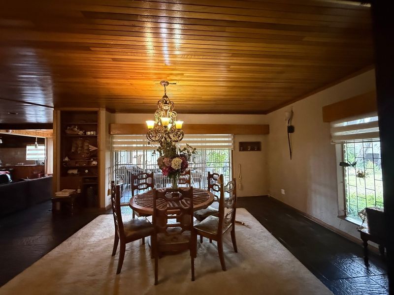 A dining room featuring a warm timber-clad ceiling, built-in shelving, and a decorative chandelier, with direct access to an outdoor area through a security gate.
