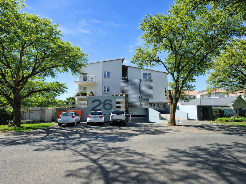 Front elevation of a modern apartment complex featuring balconies, secure driveway access, and established trees in a well-maintained residential setting.