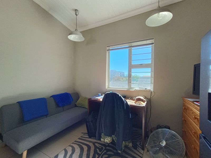 A functional bedroom featuring tiled flooring, a timber-look ceiling, and a window with security bars, offering natural light and a view of the surroundings.