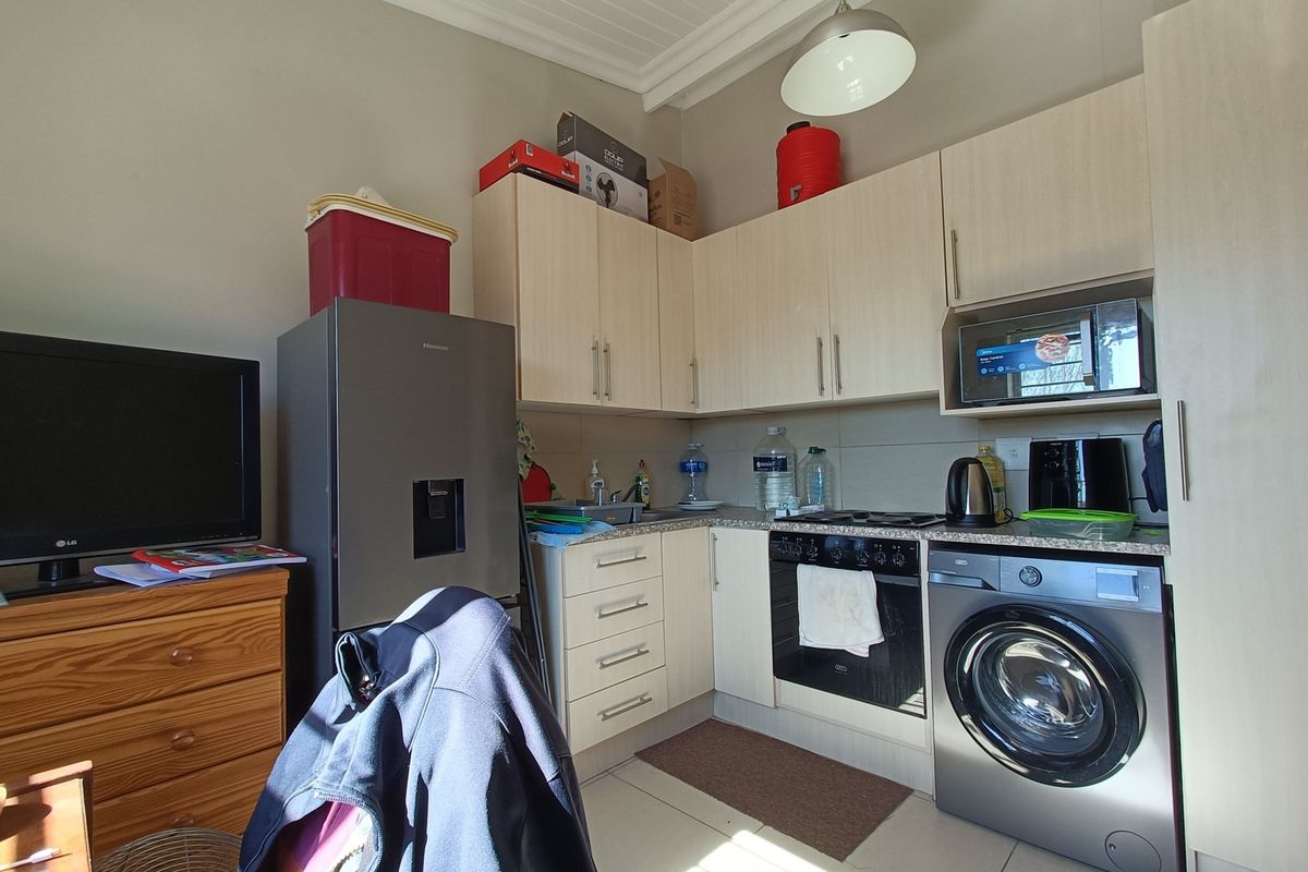 Compact kitchen featuring light wood-finish cabinetry, integrated oven and hob, tiled backsplash, and space for laundry appliances.