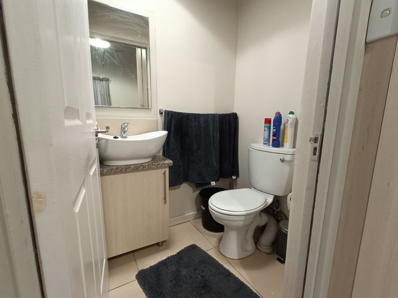A compact bathroom featuring a vessel sink with vanity cabinet, wall-mounted mirror, and standard toilet with tiled flooring.