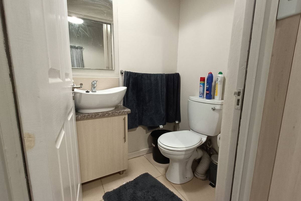 A compact bathroom featuring a vessel sink with vanity cabinet, wall-mounted mirror, and standard toilet with tiled flooring.