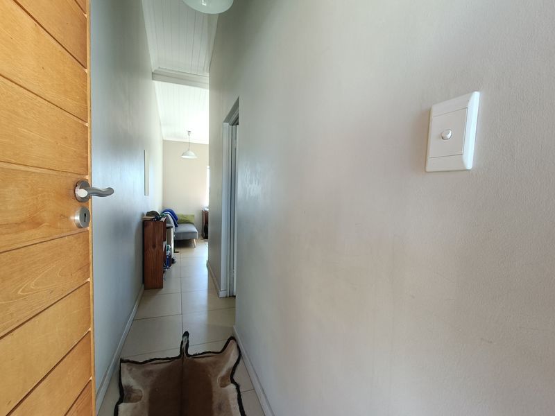 A narrow hallway featuring tiled flooring, a timber door, and a high tongue and groove ceiling, leading towards an adjacent living space.