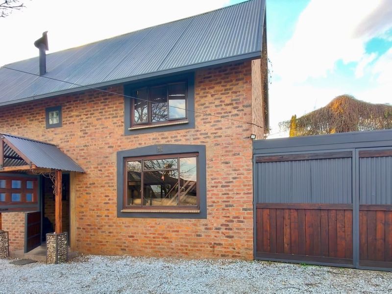 Front elevation of a charming brick house featuring a corrugated metal roof, timber-framed windows, and a covered entrance porch with a gravel driveway.