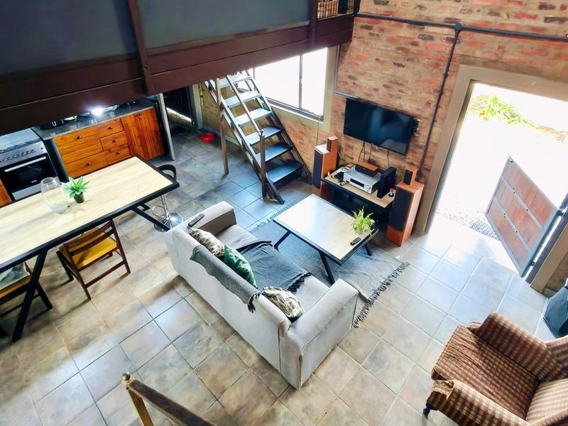 An open-plan living and kitchen area featuring exposed brick walls, tiled flooring, a mezzanine level, and a wood-burning stove.