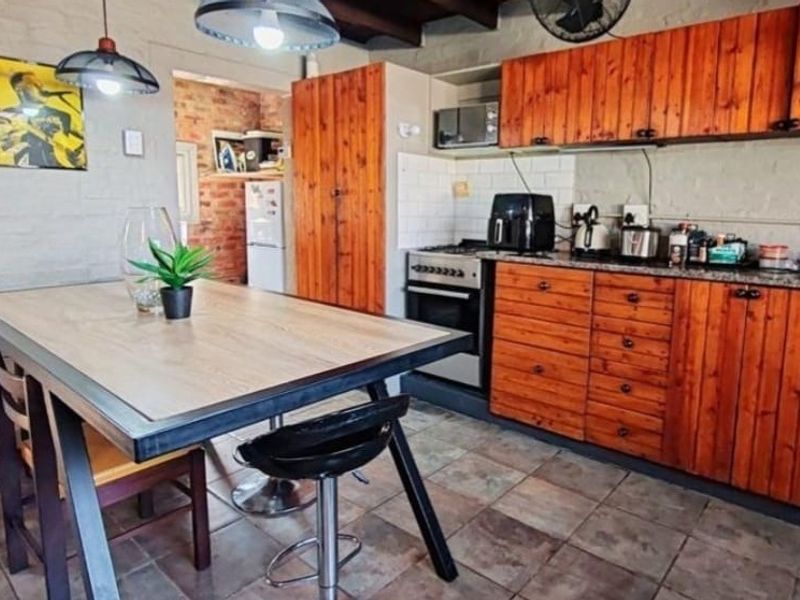 Open-plan kitchen and dining area featuring rustic wooden cabinetry, stone countertops, built-in appliances, and tiled flooring with exposed brick wall accents.