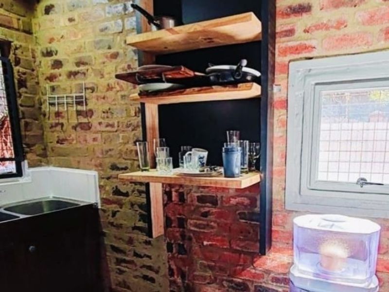 A rustic scullery area featuring exposed brick walls, a double sink with mixer tap, and custom built-in wooden shelving.