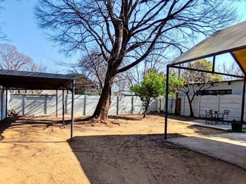 Spacious backyard featuring a precast concrete boundary wall, metal carport structures, and a concrete patio area, offering significant potential for landscaping.