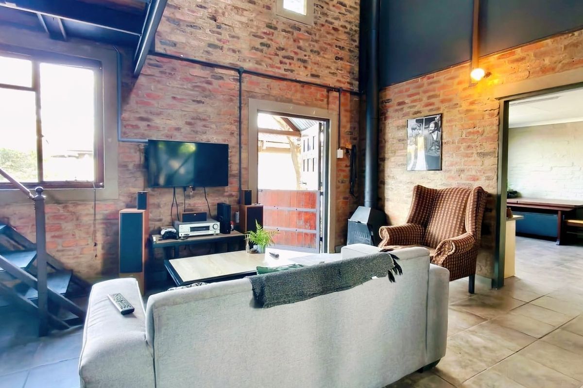 A rustic living room featuring exposed brick walls, a wood-burning fireplace, and a staircase, creating a warm and industrial-style atmosphere.