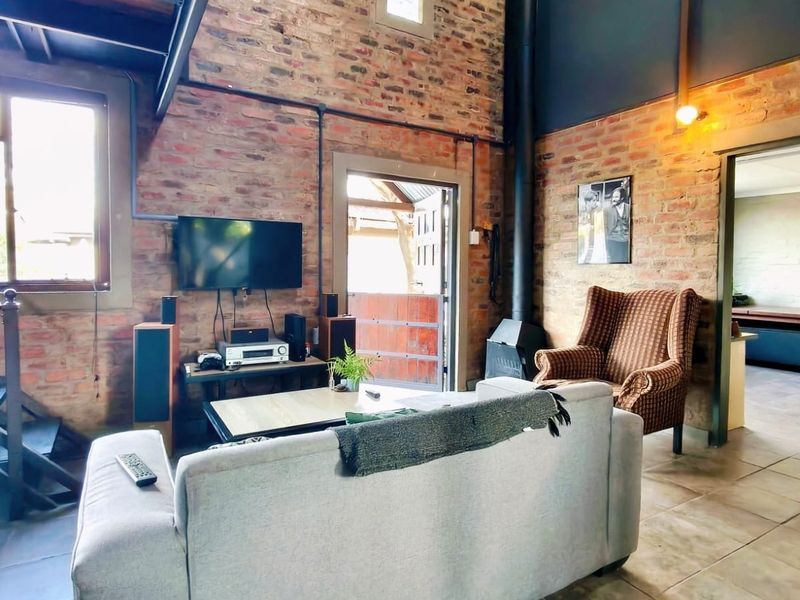 A rustic living room featuring exposed brick walls, a wood-burning fireplace, and a staircase, creating a warm and industrial-style atmosphere.