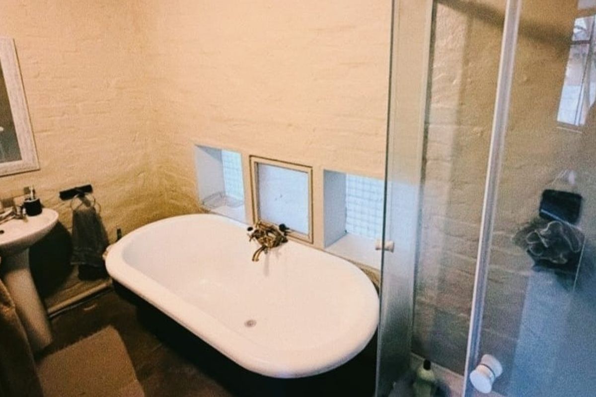 A bathroom featuring a freestanding bathtub, pedestal basin, and a glass-enclosed shower, set against textured exposed brick walls with glass block windows.