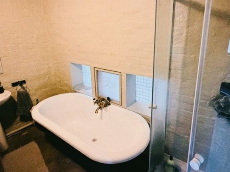 A bathroom featuring a freestanding bathtub, pedestal basin, and a glass-enclosed shower, set against textured exposed brick walls with glass block windows.