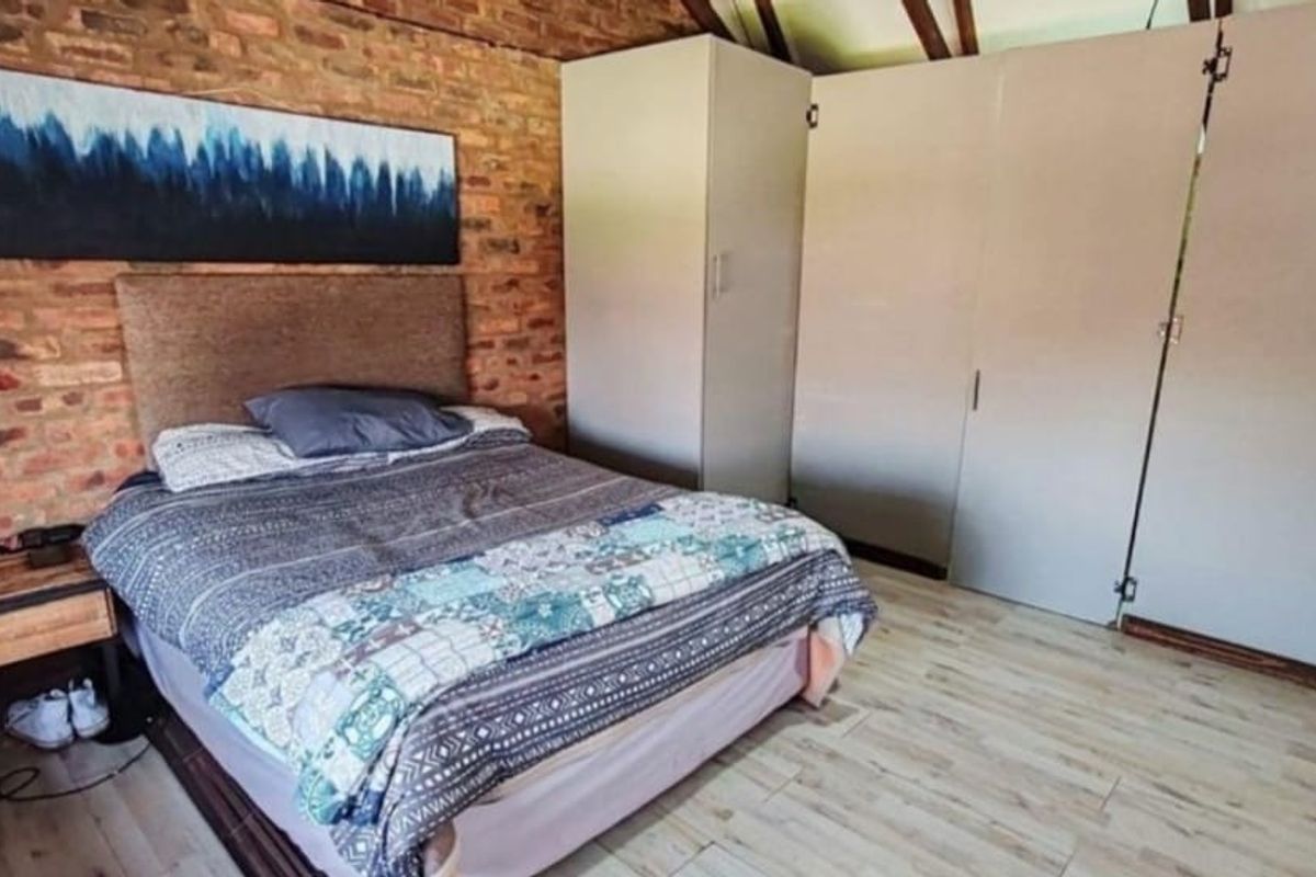 Bedroom featuring an exposed brick feature wall, built-in storage cupboards, and laminate flooring under exposed timber rafters.