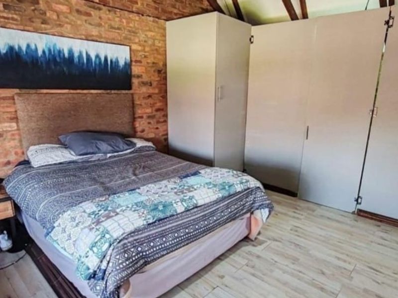 Bedroom featuring an exposed brick feature wall, built-in storage cupboards, and laminate flooring under exposed timber rafters.