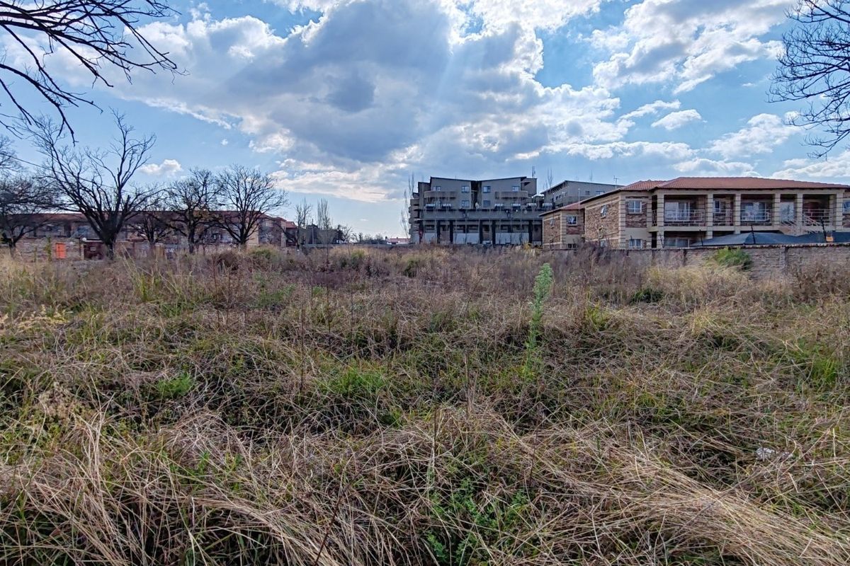 A vacant residential plot featuring overgrown grass and a boundary wall, situated in a developed neighborhood setting.