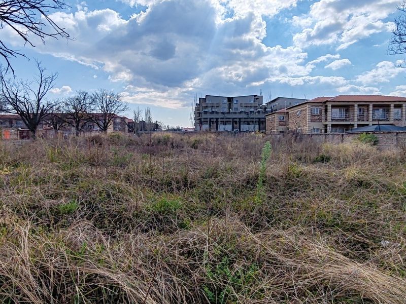 A vacant residential plot featuring overgrown grass and a boundary wall, situated in a developed neighborhood setting.