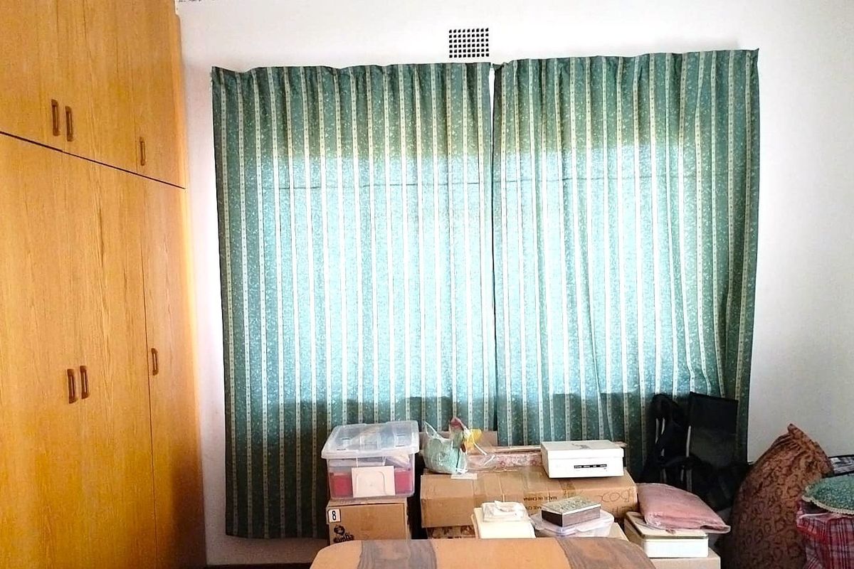 A bedroom featuring floor-to-ceiling wooden built-in cupboards and a window with curtains.