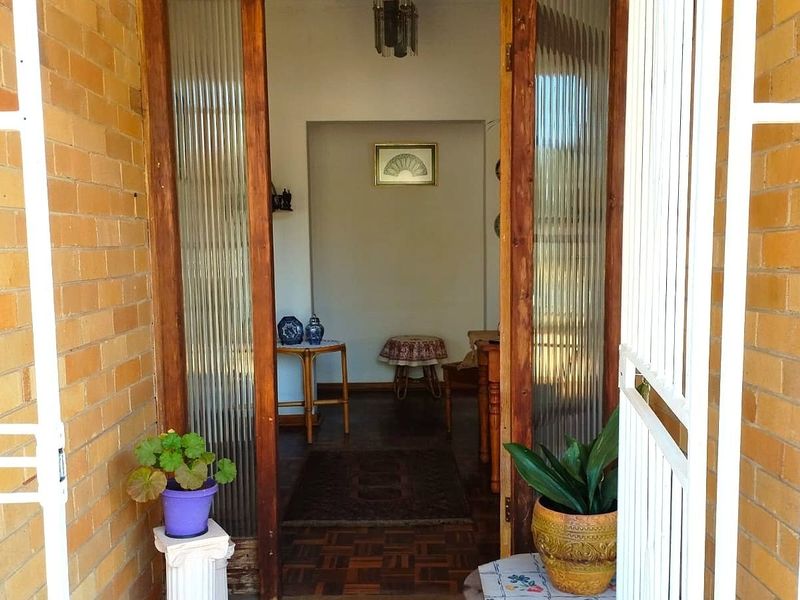 Entrance area featuring a brick facade, security gate, and fluted glass double doors leading into a home with parquet flooring.