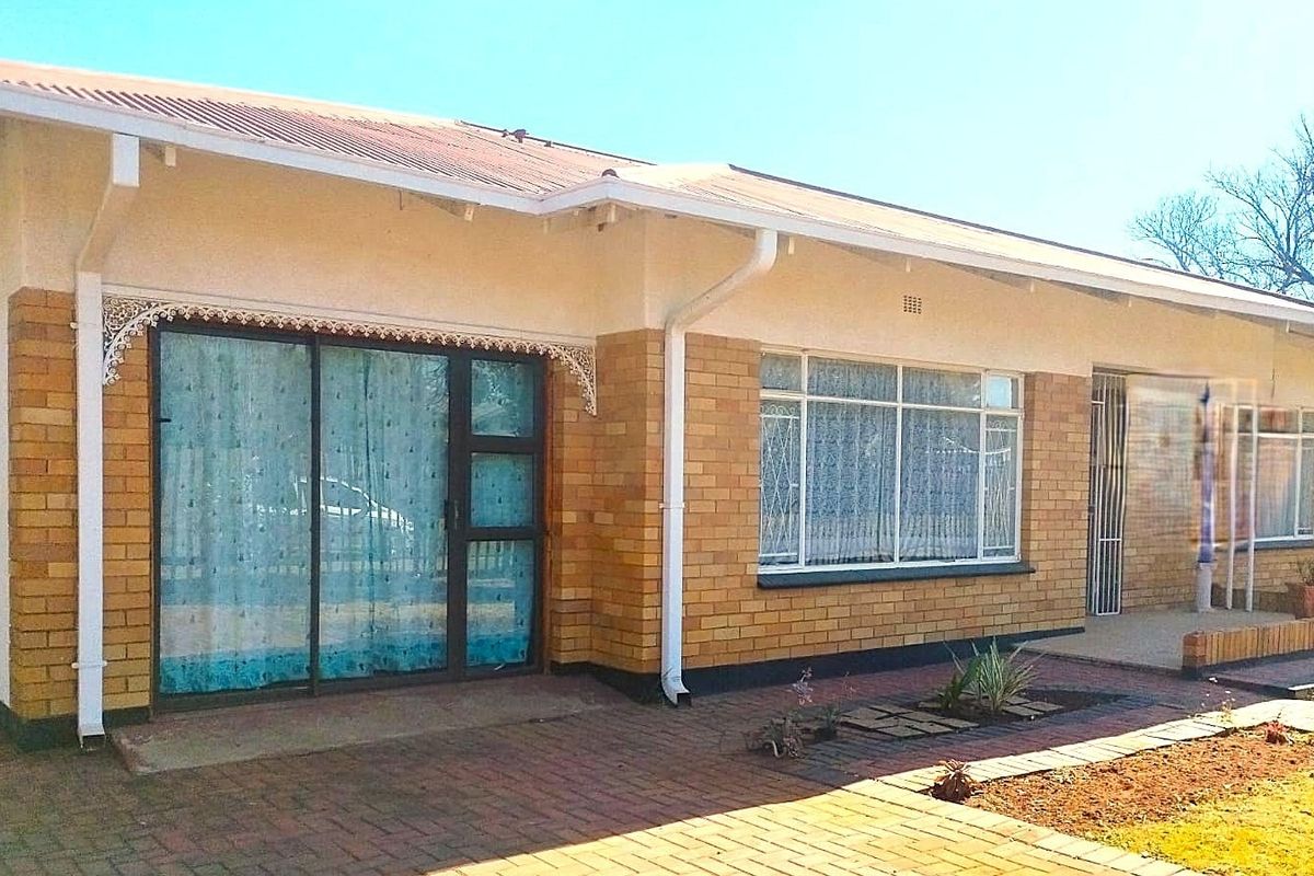 Rear view of a single-story brick house featuring a paved patio area, sliding glass doors, and a metal roof.