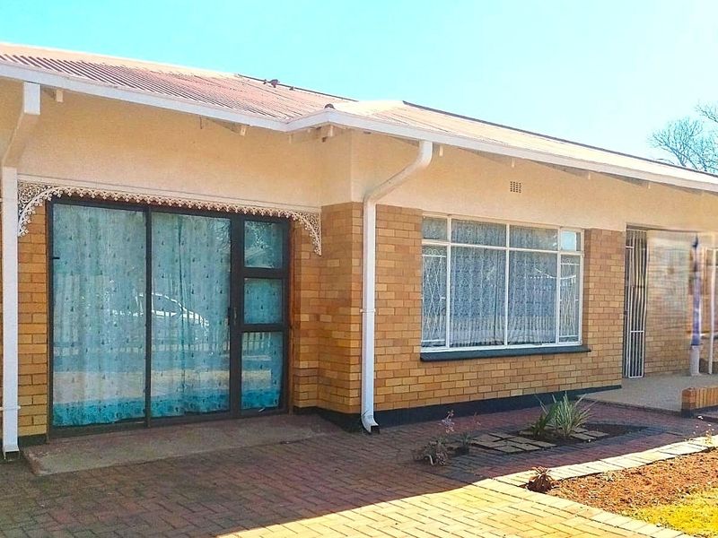 Rear view of a single-story brick house featuring a paved patio area, sliding glass doors, and a metal roof.