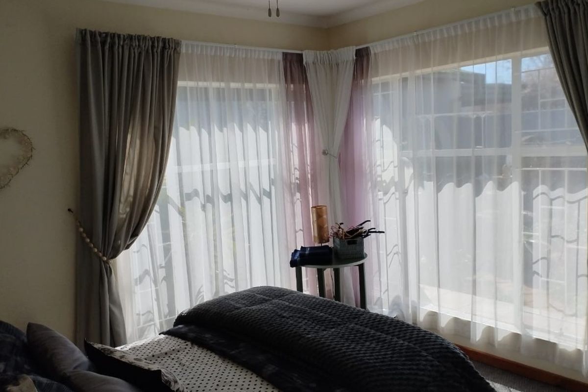 A bedroom featuring corner windows with layered curtains, providing natural light and a view of the exterior.