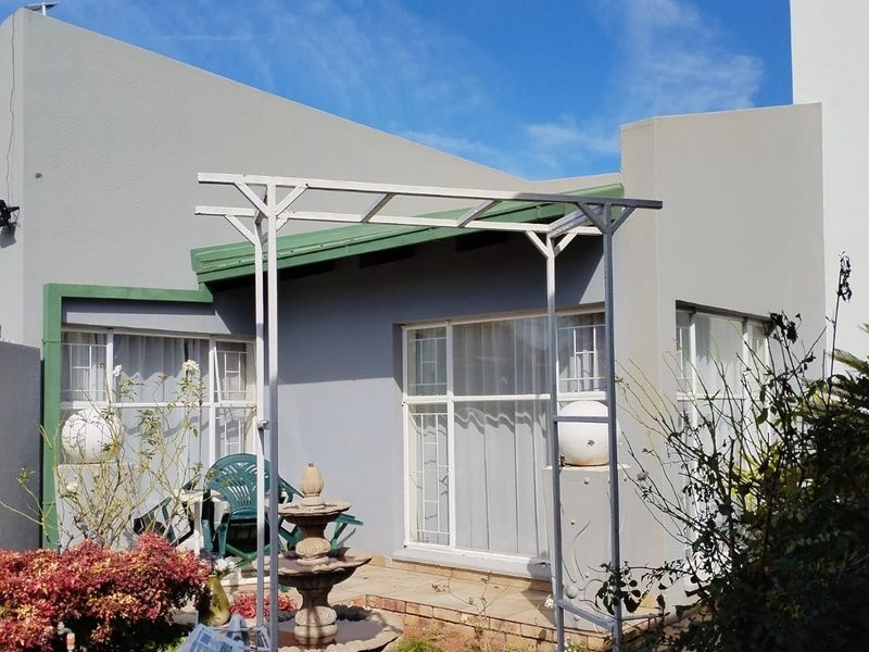 Rear exterior view of the house featuring a paved patio area, metal pergola structure, and aluminium framed windows with security bars.
