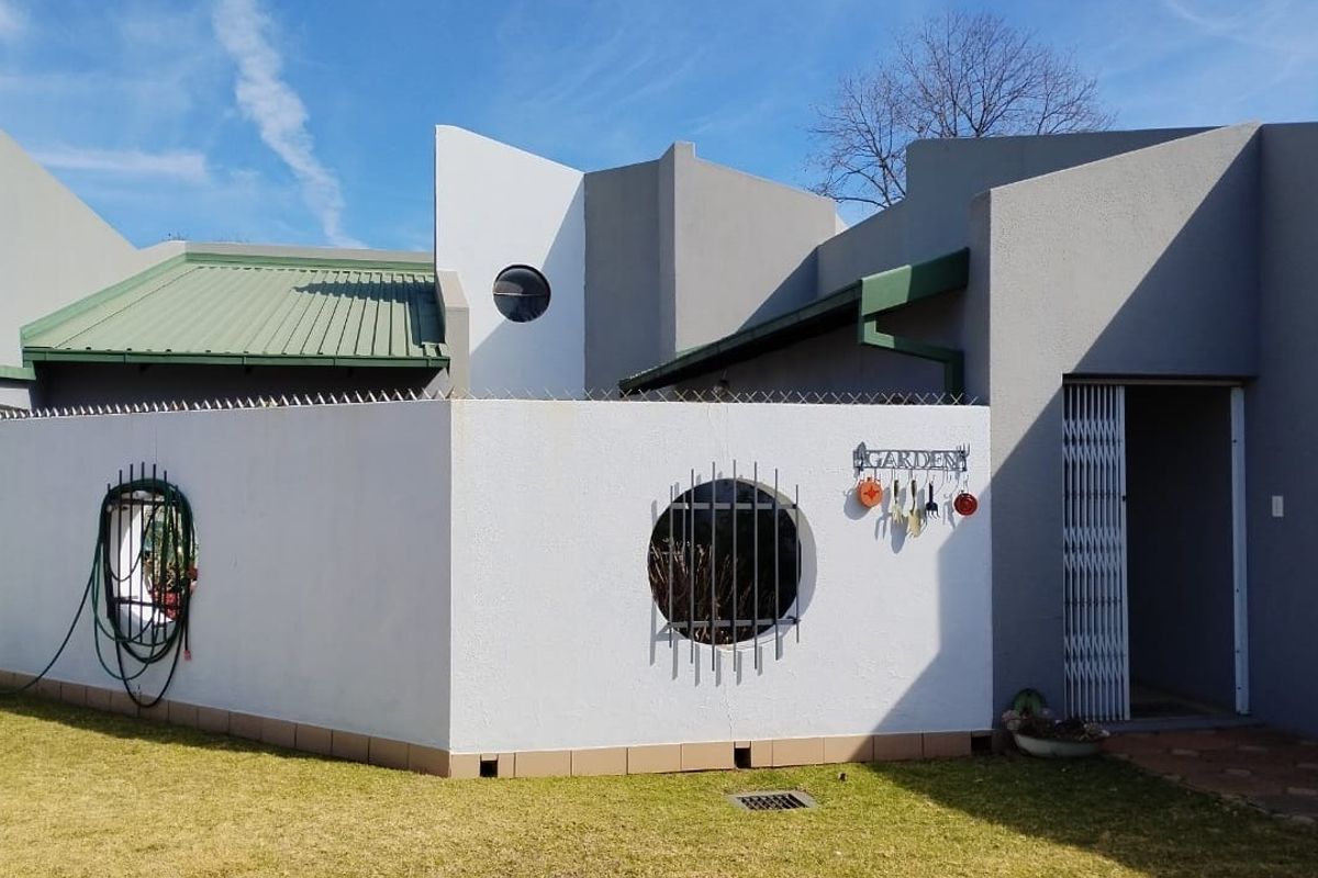 Rear exterior view of the property featuring a modern architectural design with a circular window, security gate, and well-maintained exterior walls.