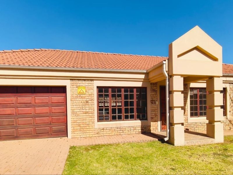 Front elevation of a face brick townhouse featuring a tiled roof, single garage with wooden door, and a paved driveway.