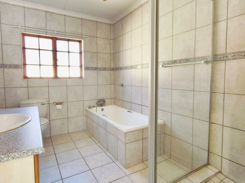 A functional bathroom featuring a built-in vanity, bathtub, separate shower enclosure, and neutral ceramic tiling throughout.
