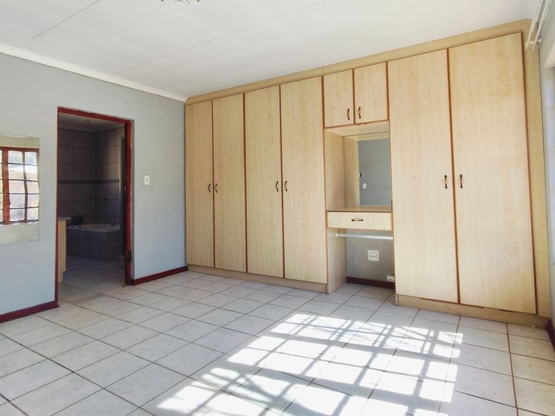 Spacious bedroom featuring extensive built-in cupboards with an integrated vanity, tiled flooring, and large wooden-framed windows allowing for ample natural light.