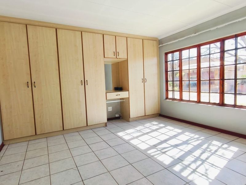 A spacious bedroom featuring light wood built-in cupboards with an integrated vanity, tiled flooring, and large windows allowing for ample natural light.
