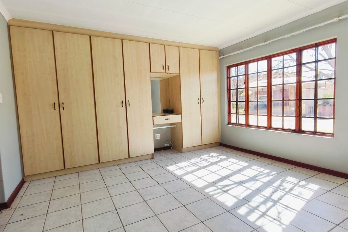 A spacious bedroom featuring light wood built-in cupboards with an integrated vanity, tiled flooring, and large windows allowing for ample natural light.